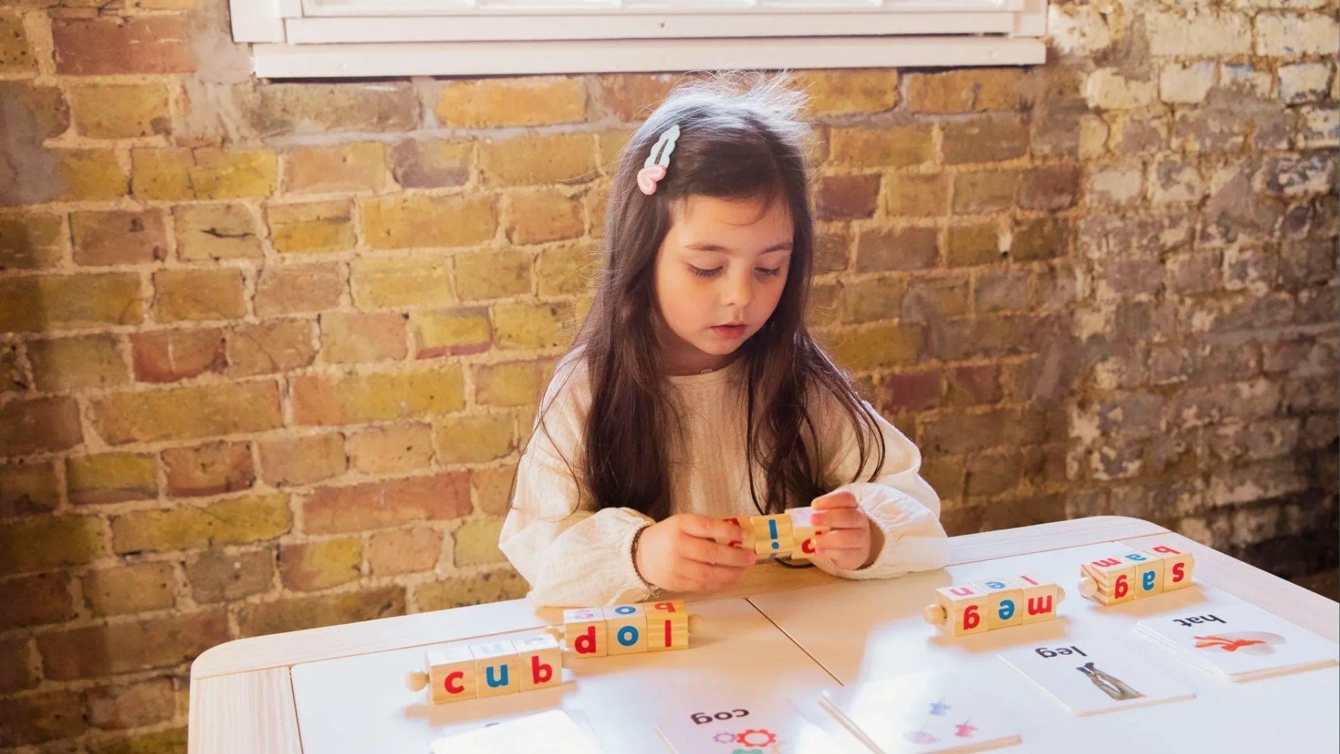 Young girl focuses on wooden letter blocks spelling words like cub and loop at table with cards