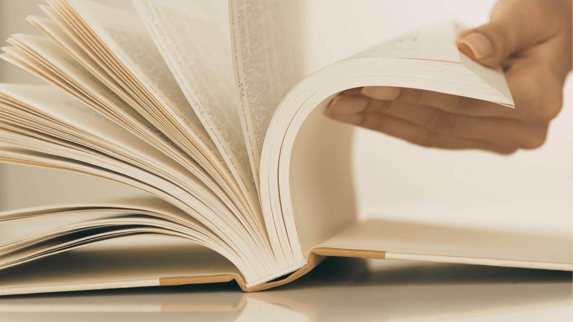 Close-up of a hand flipping through pages of an open book with warm lighting.