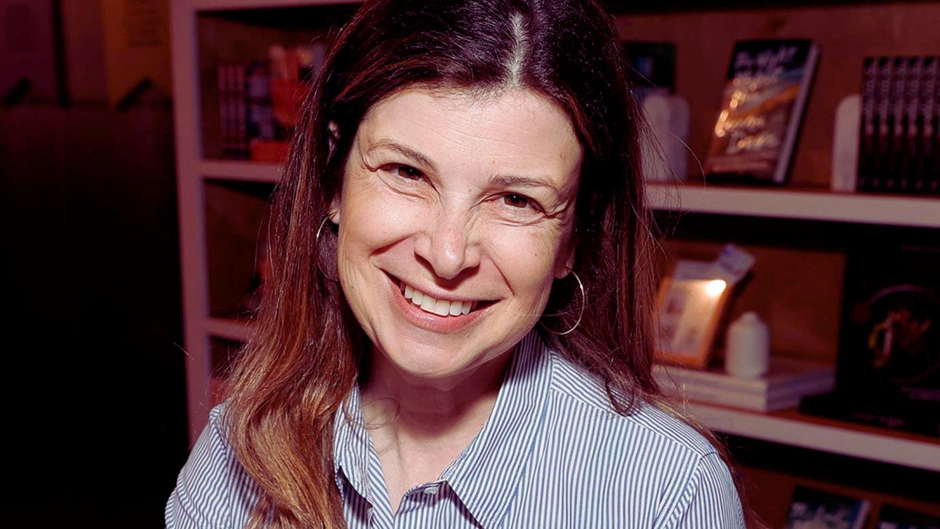A woman smiles at the camera, standing in front of a bookshelf filled with various books.
