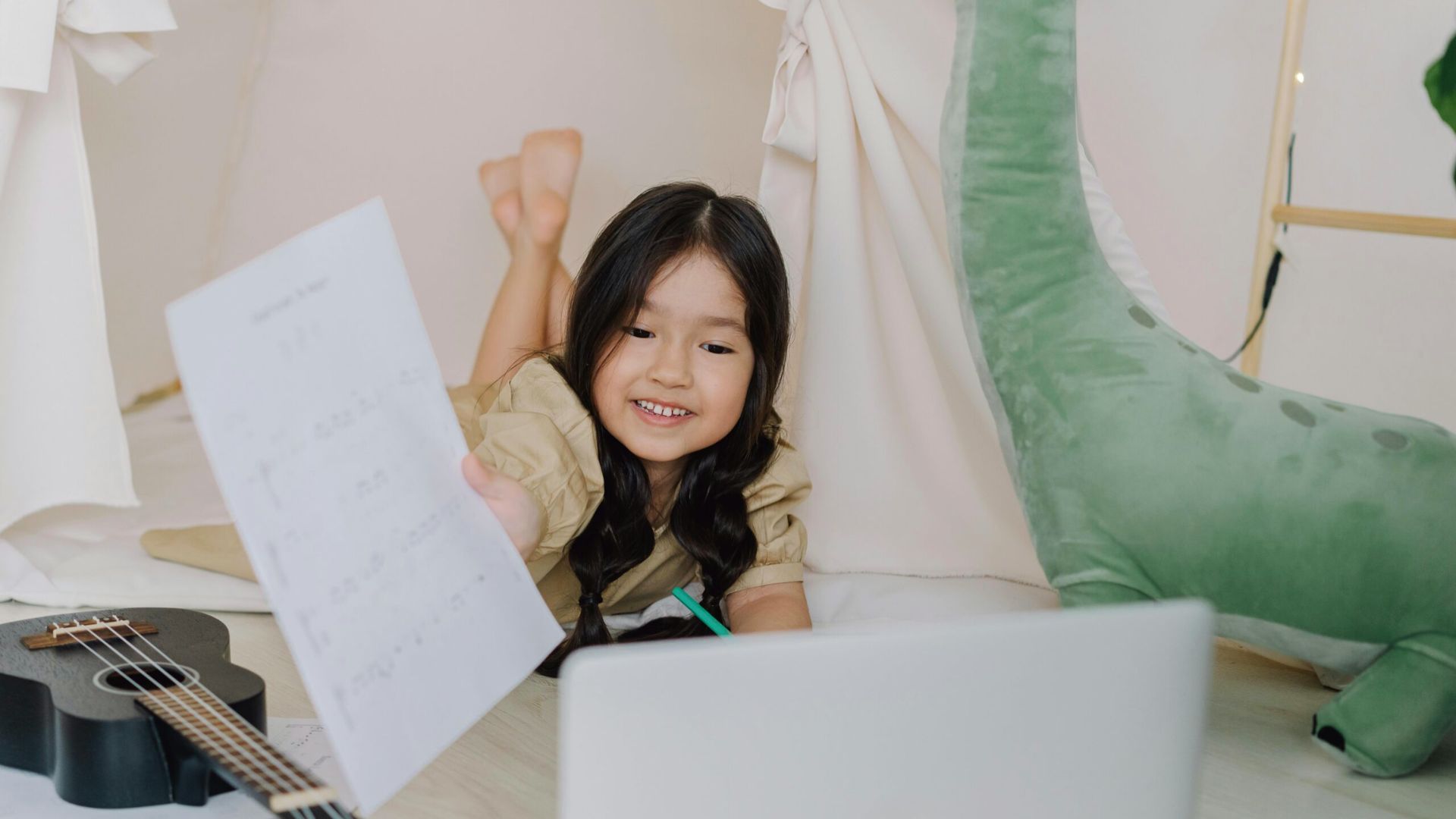 A young girl on her bed with a guitar and laptop, focused on her studies through accredited homeschool programs.