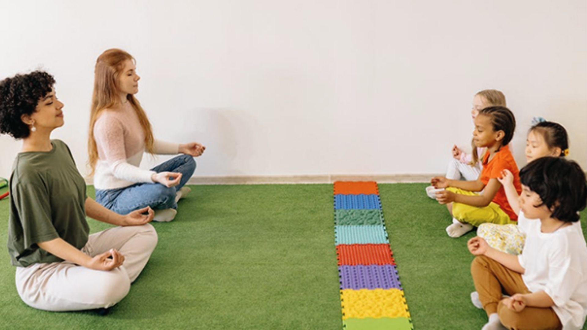 Kids and adults meditate cross-legged on green mat, showing mindfulness breaks reduce homework stress.