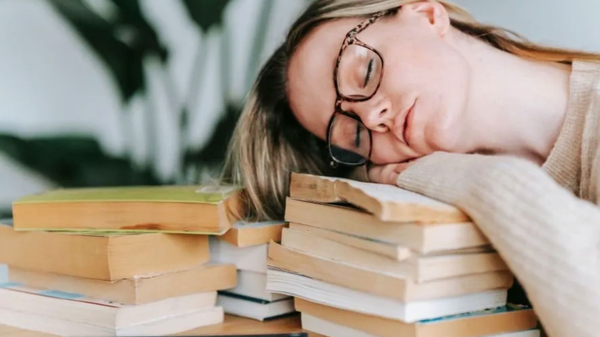 A woman dozing atop a pile of books, illustrating the struggle many adults face in developing a regular reading habit.