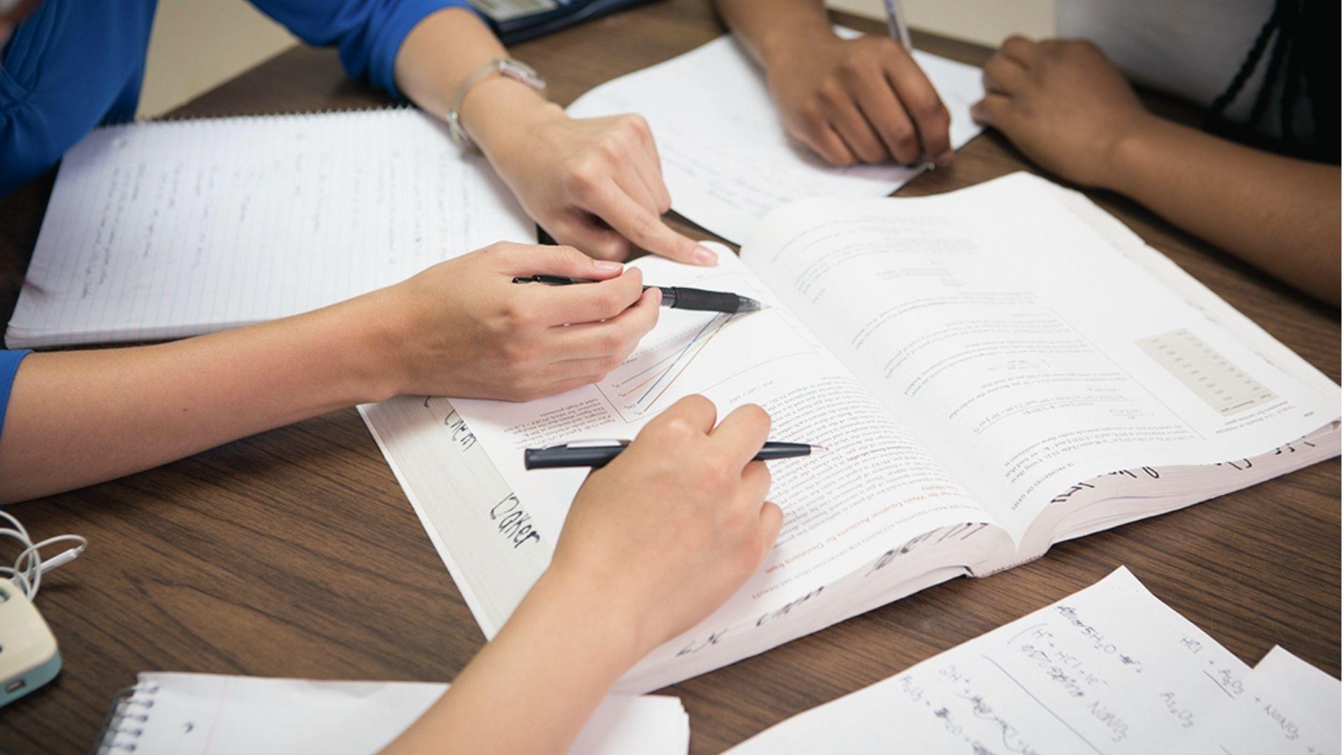 Group study with students pointing at textbooks, proving peer support helps tackle homework procrastination.