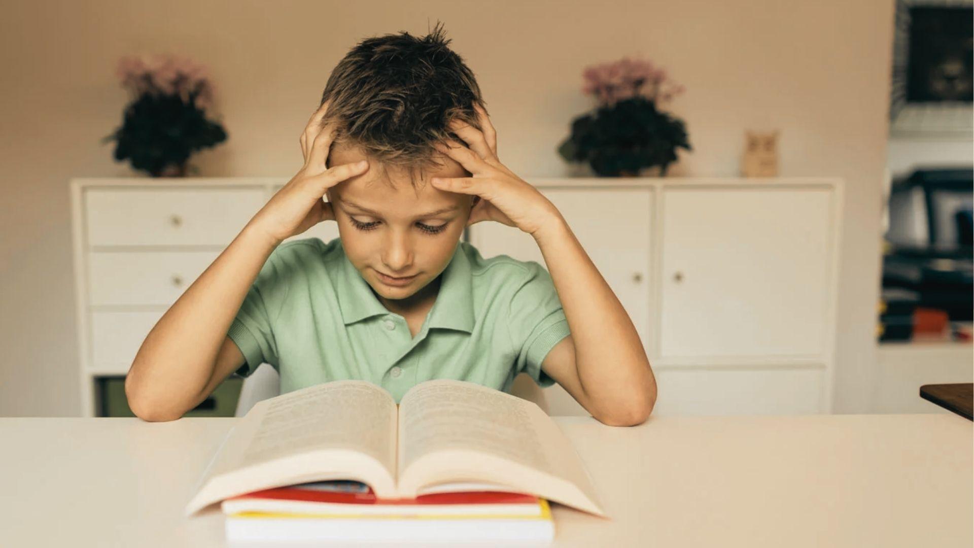 A young girl sits on a couch with an adult, concentrating hard as she reads a book