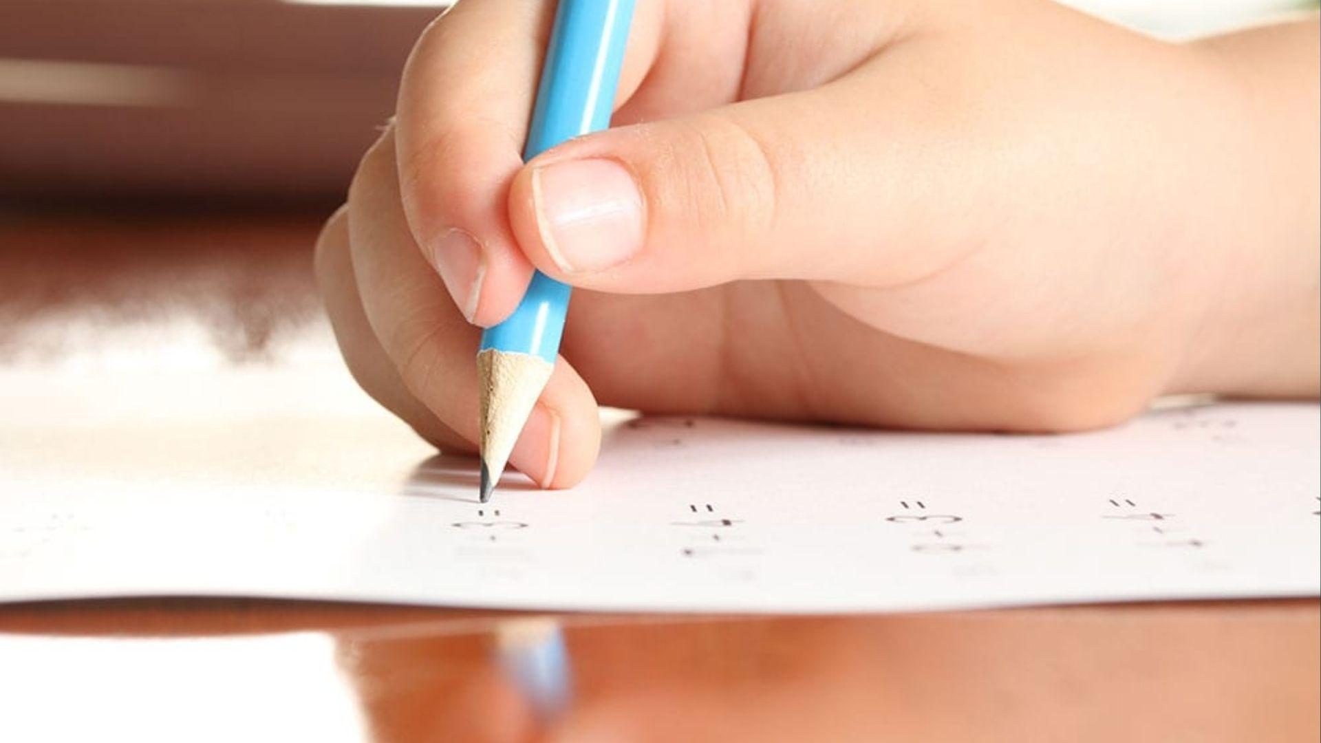 Close-up of child’s hand with blue pencil writing, showing proper grip boosts writing neatness.