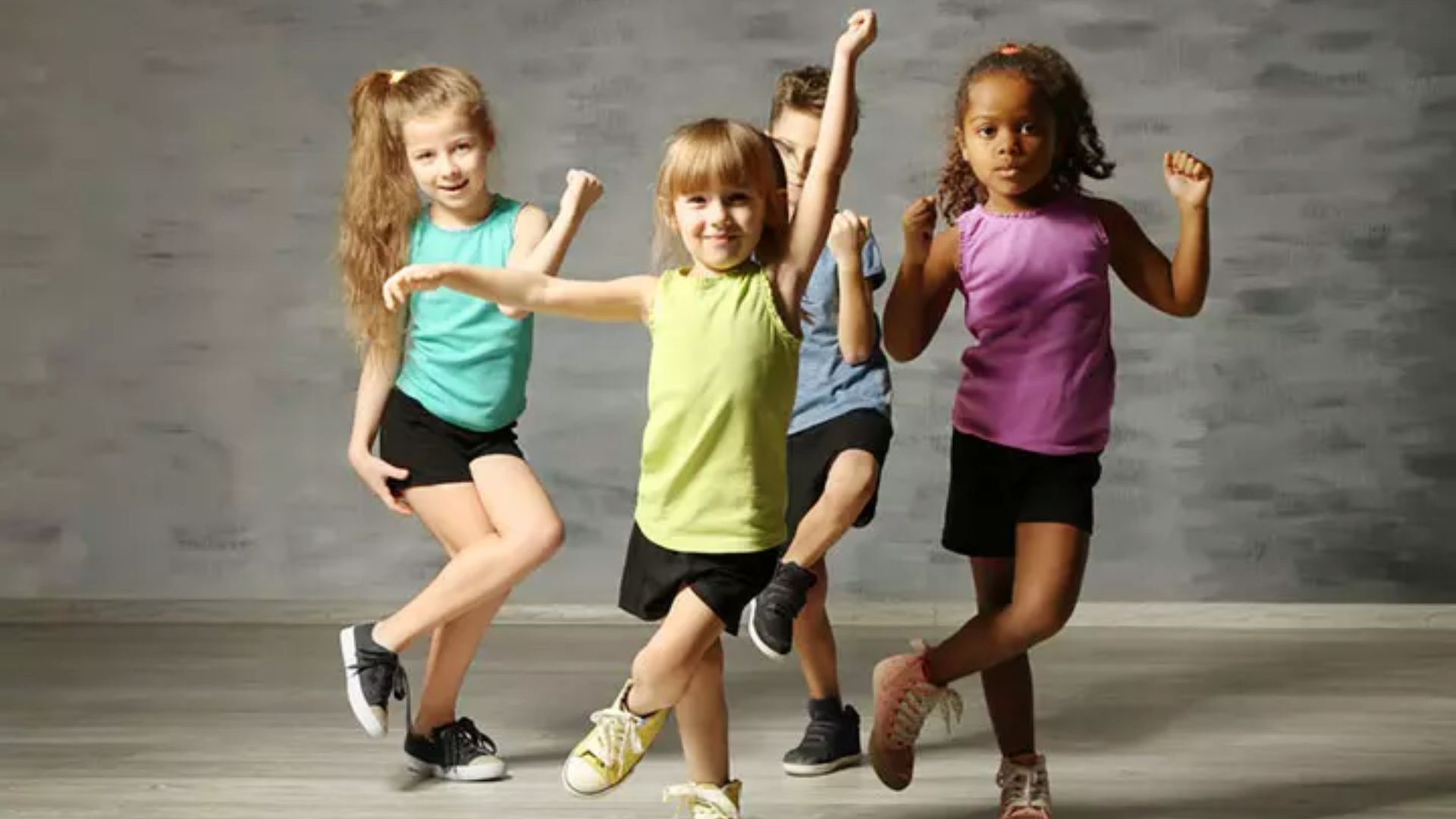 Four kindergarteners dance and strike fun poses together in a bright movement class.