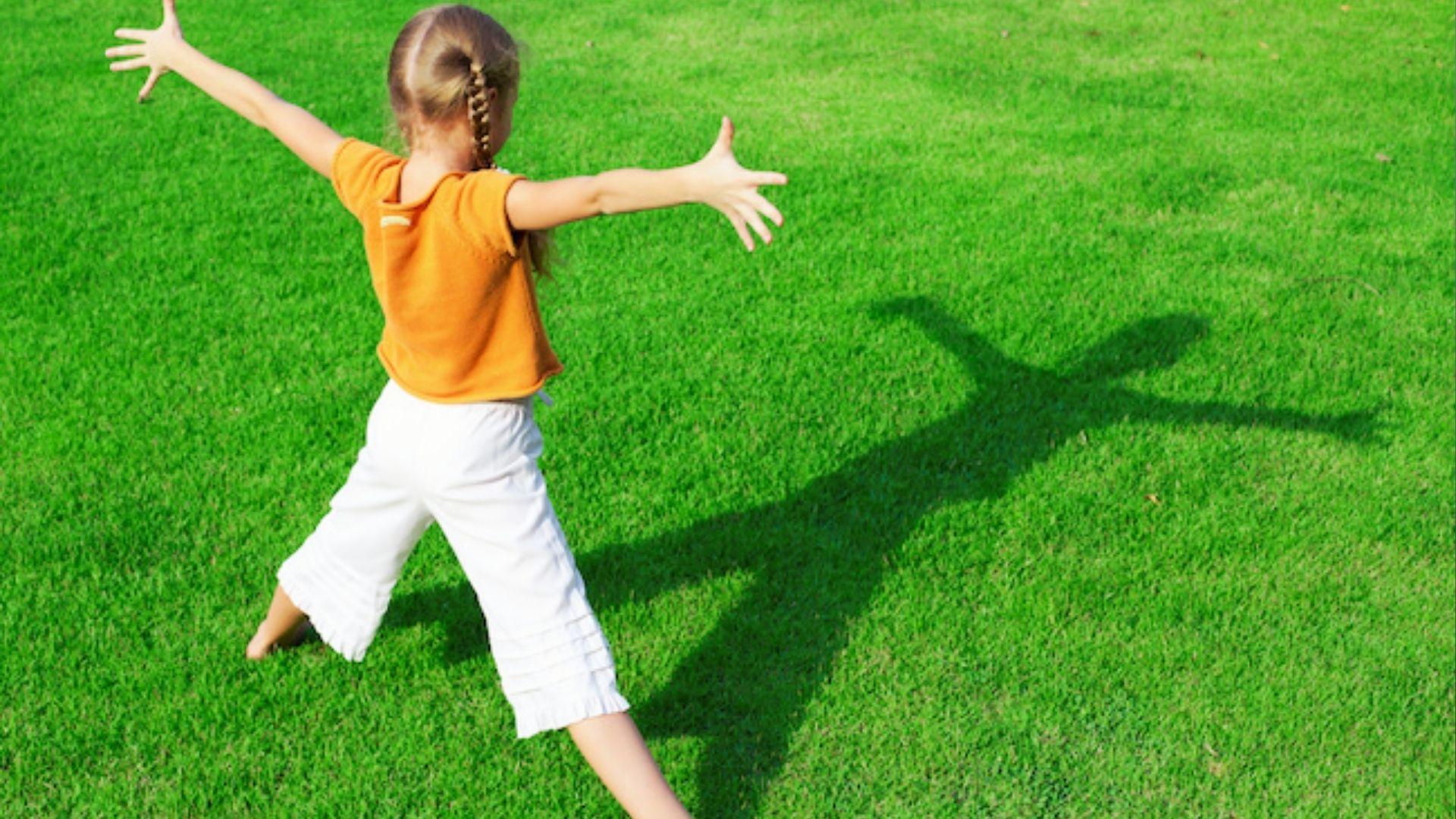 Girl in orange shirt stretches on grass forming letters with her body for outdoor spelling fun