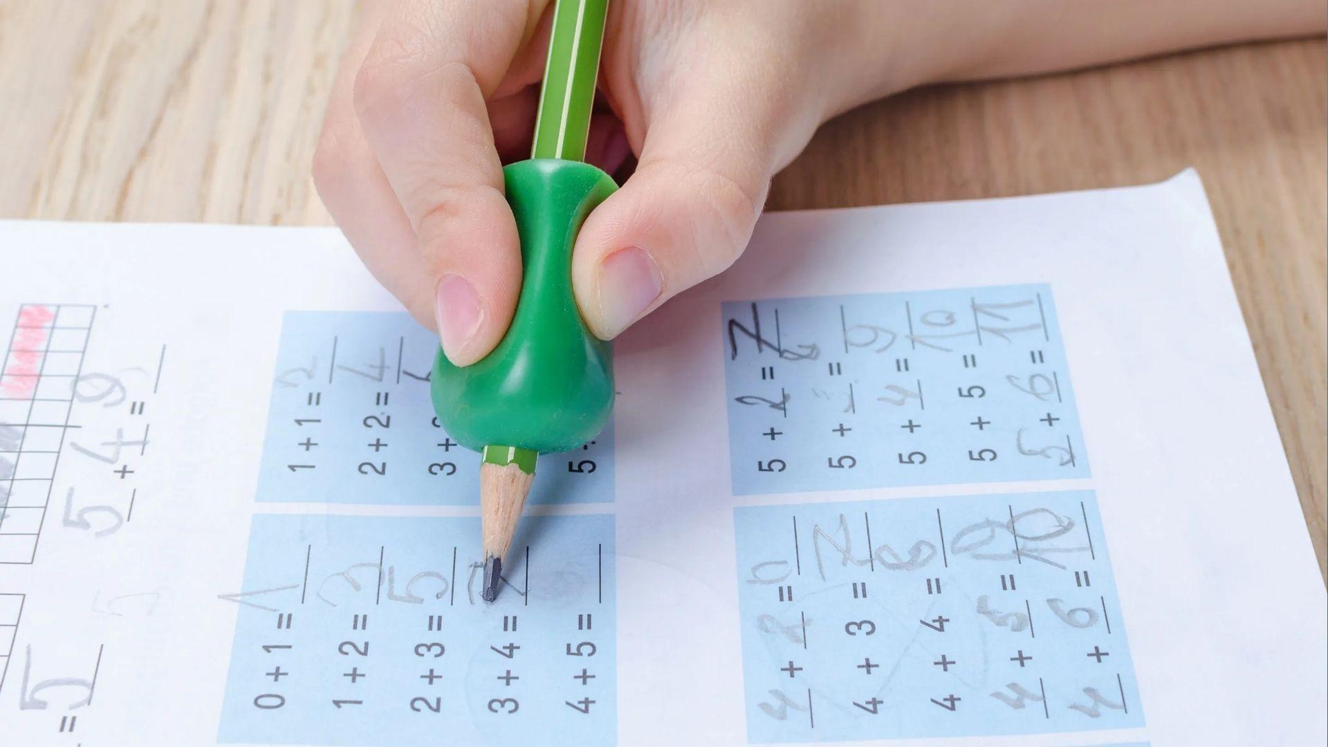 The kid uses a green pencil grip on the worksheet to solve math, improving control and letter formation.