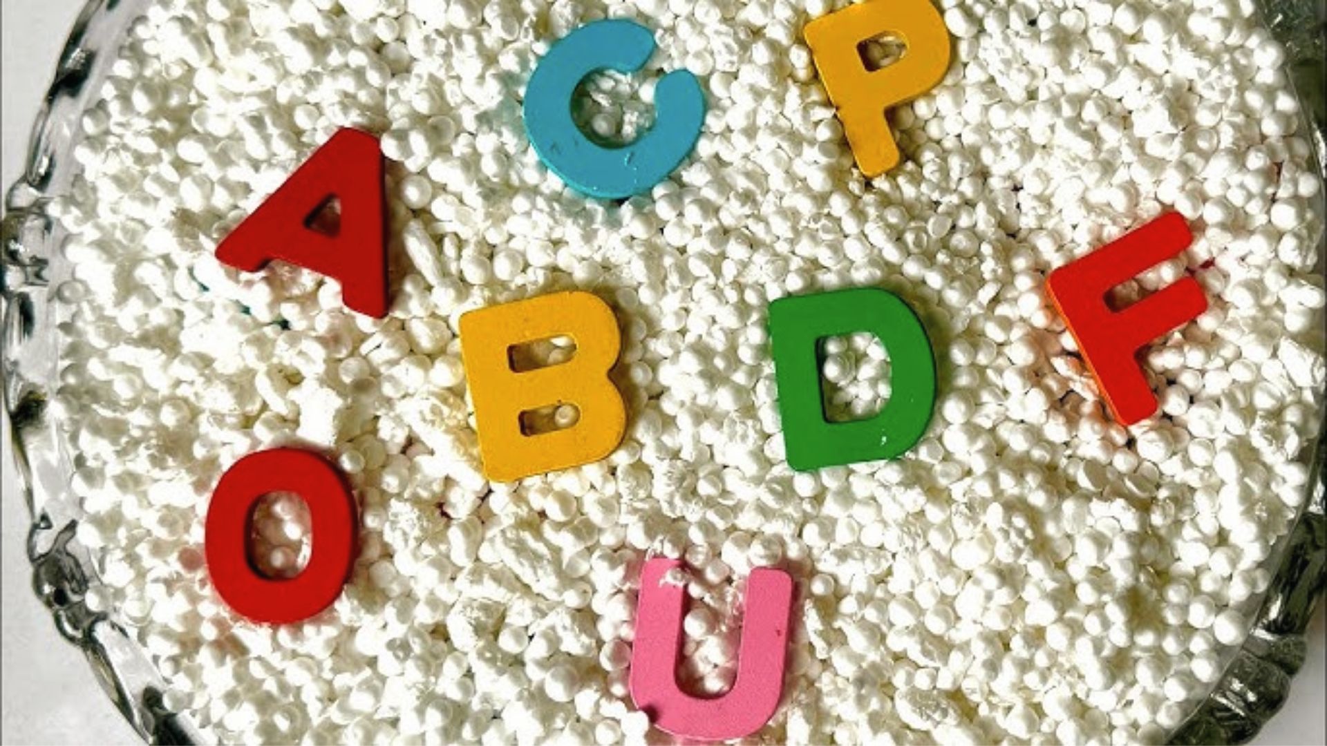 Colorful wooden letters are scattered in a tray of white sensory beads for kids to find.