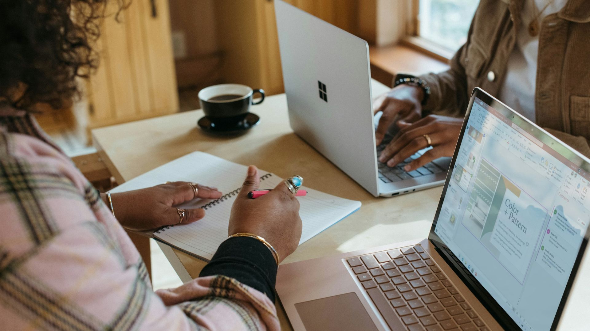 Two students collaborate on a project using laptops and handwritten notes at a shared table.