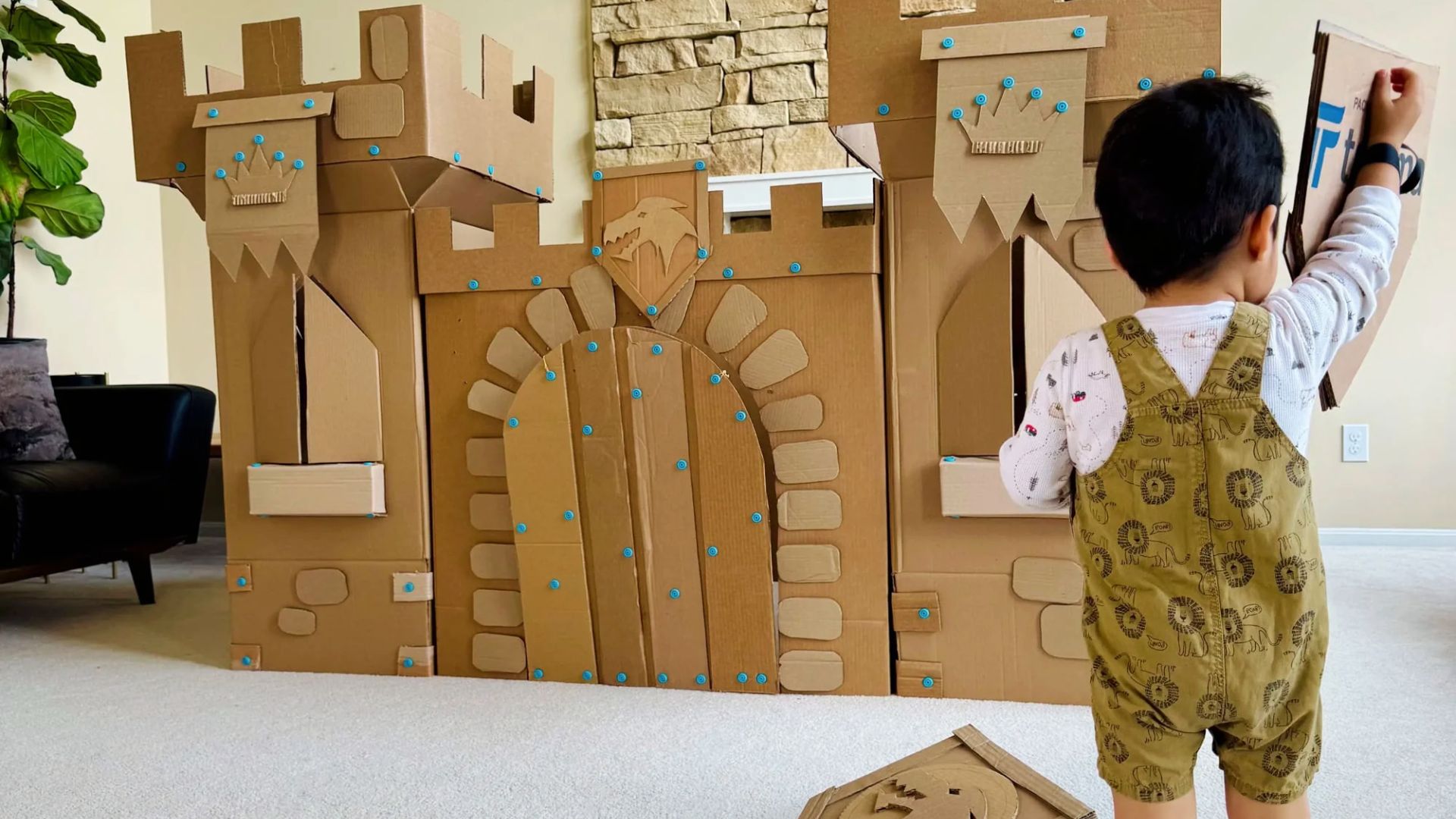 A child in overalls adds a piece to a large cardboard castle during creative play.