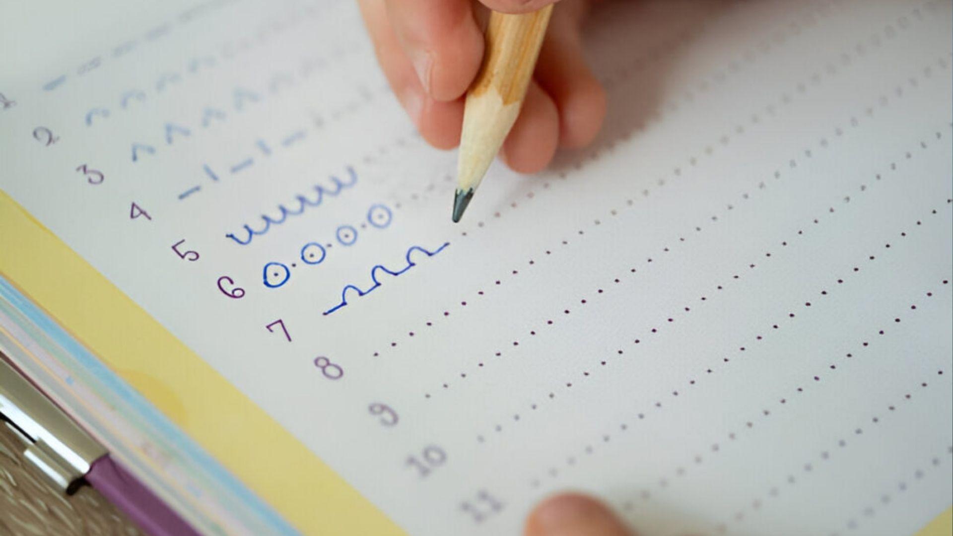 The pencil traces dotted lines and curves in the workbook, building fine motor skills for handwriting.