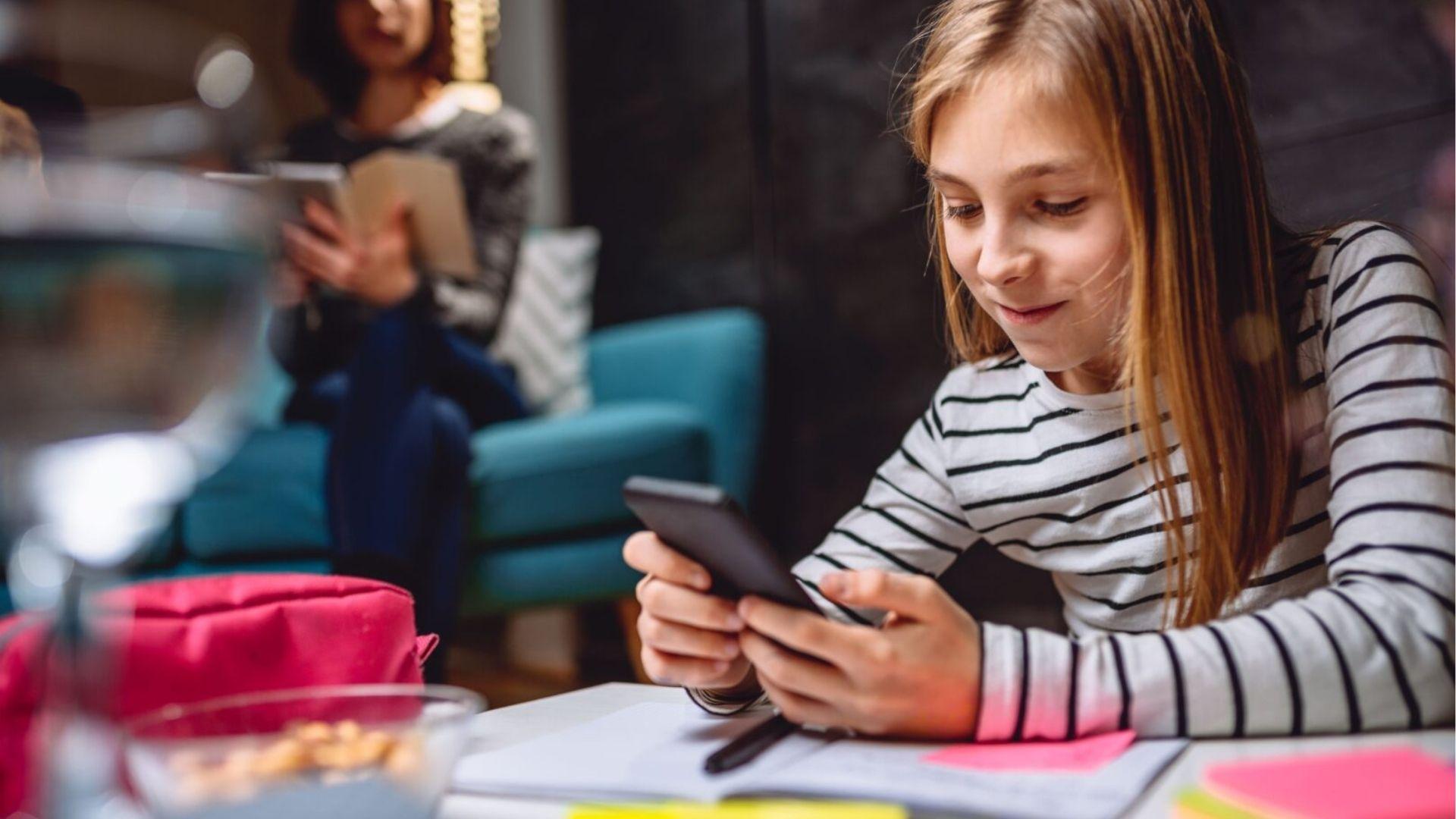 Girl uses phone near homework , highlighting digital distractions that cause study procrastination.