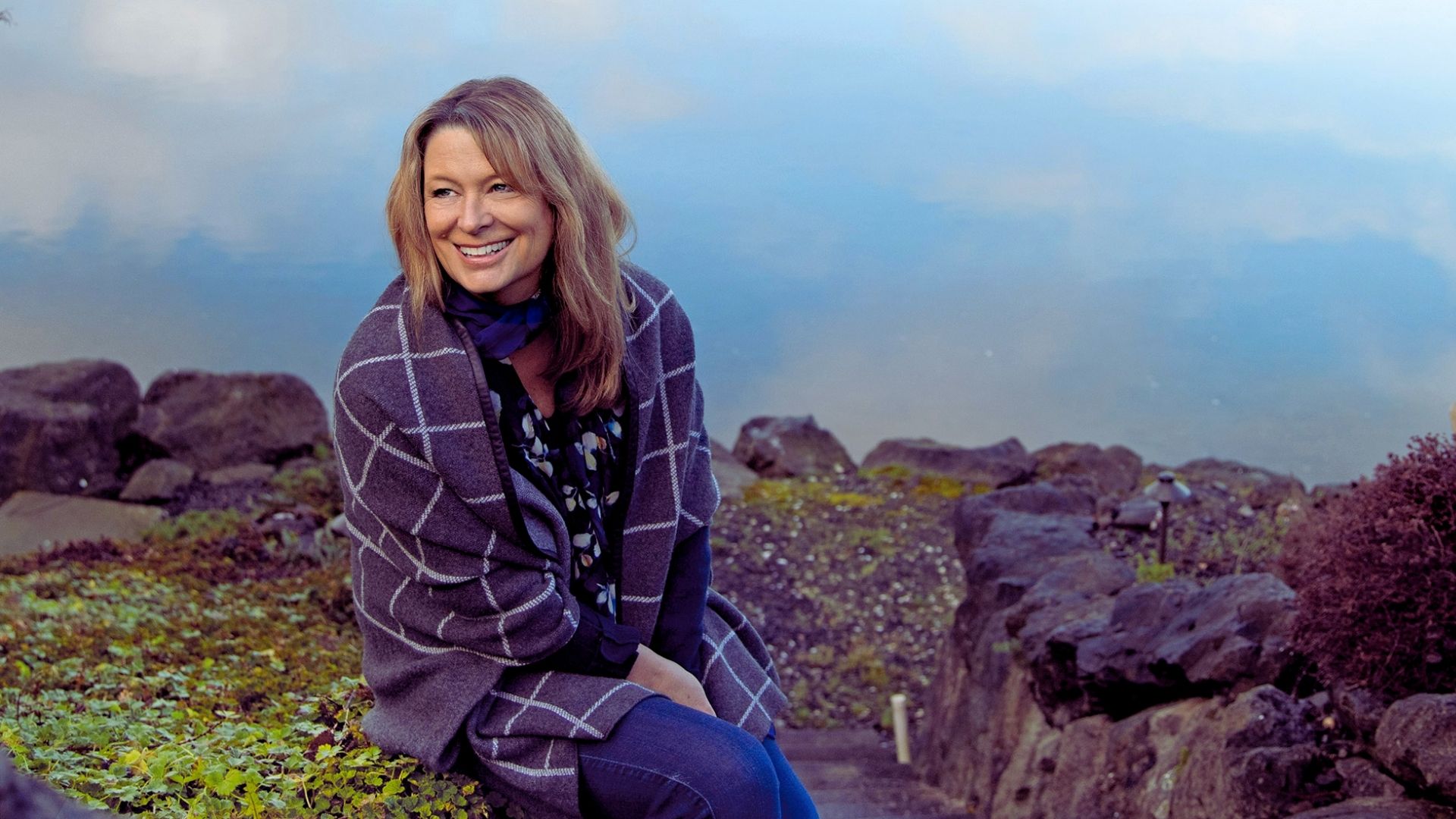 A woman sitting on a rock by the water, gazing thoughtfully at the serene landscape around her.