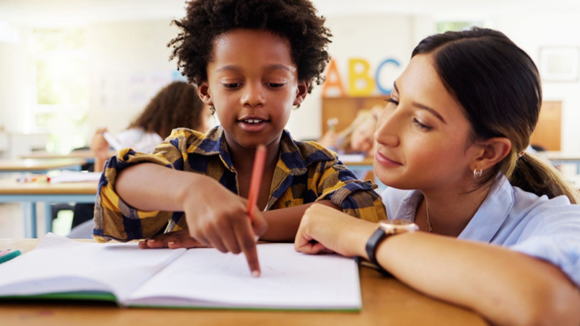 A teacher guides a child through homework, emphasizing reading encoding techniques for better understanding