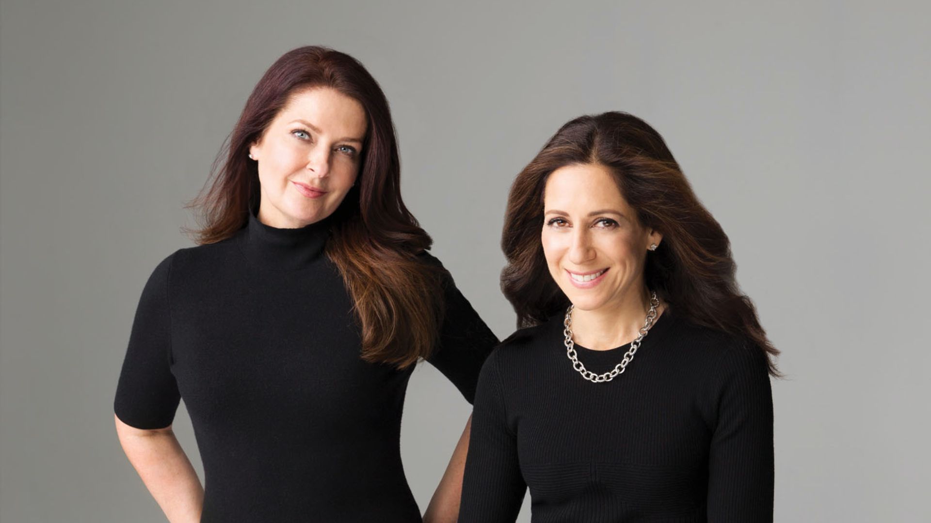 Authors Greer Hendricks and Sarah Pekkanen, two women in black shirts, standing closely together.