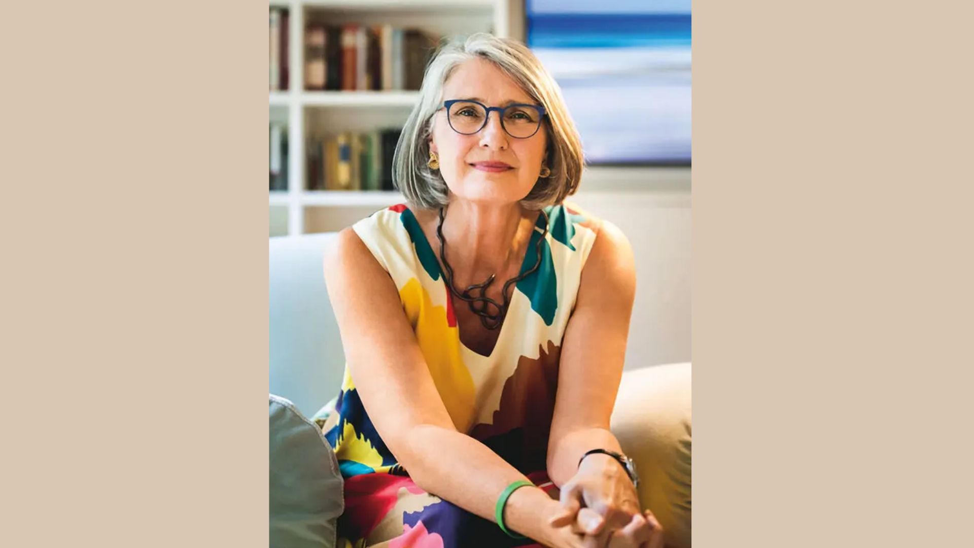 “louise Penny”wearing glasses is sitting comfortably on a couch, looking relaxed and engaged in her surroundings.