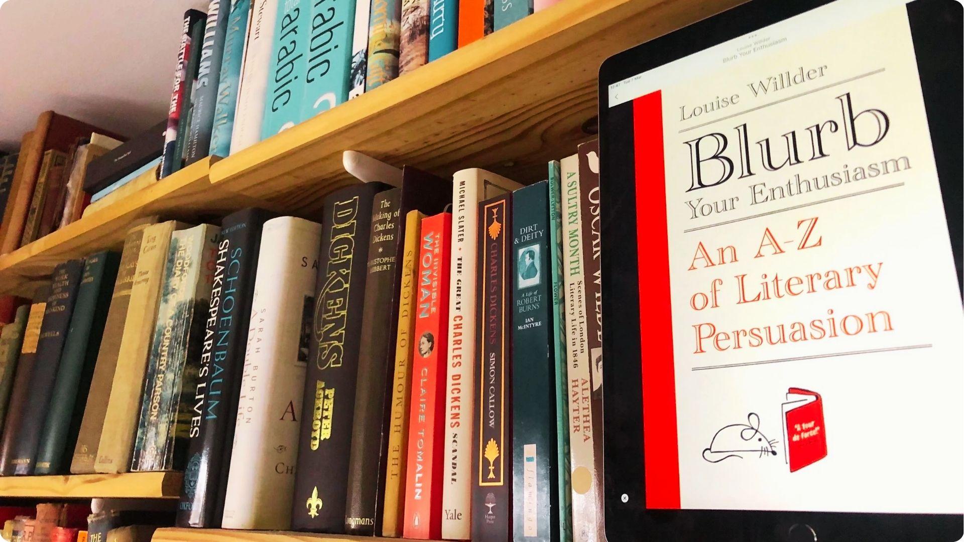 Tablet displaying Blurb Your Enthusiasm: An A-Z of Literary Persuasion by Louise Willder, placed in front of wooden bookshelves.