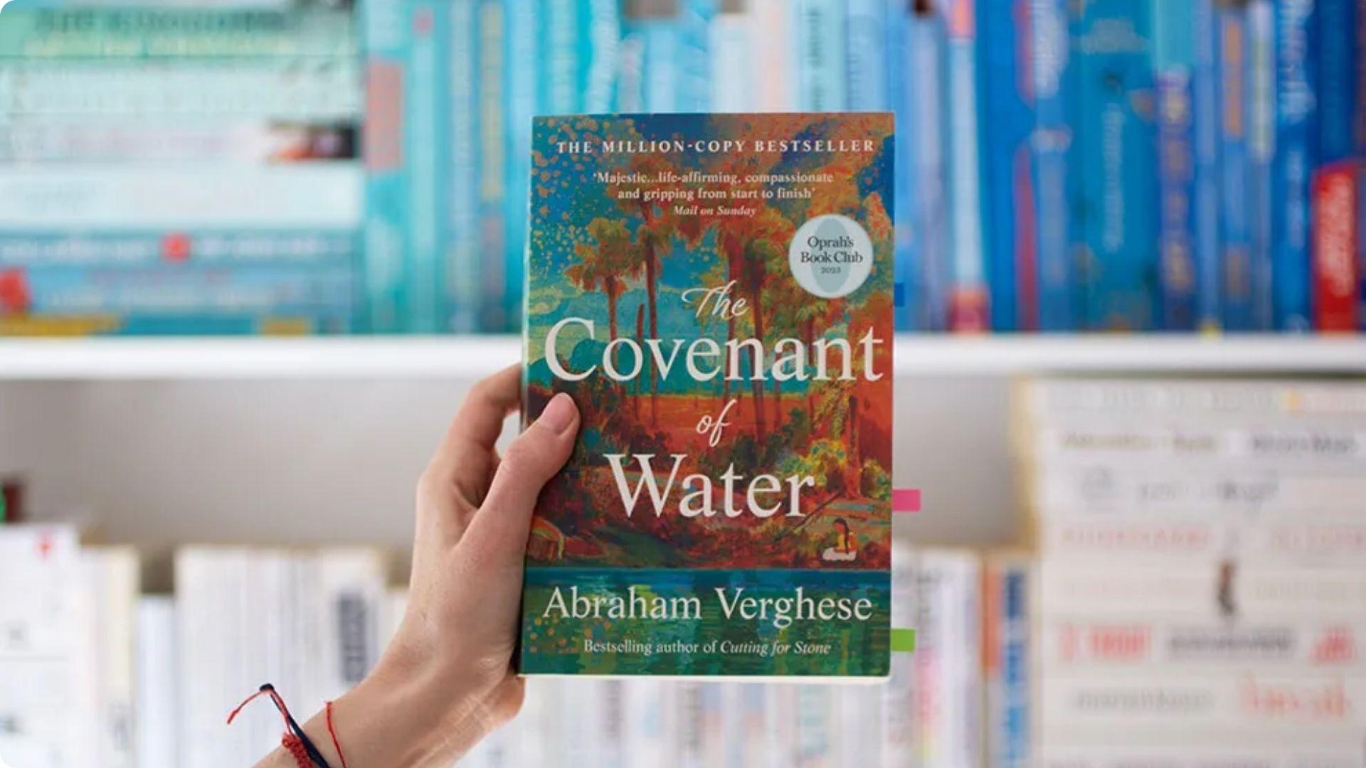 Hand holding "The Covenant of Water" by Abraham Verghese, an Oprah's Book Club pick, in a bookstore.