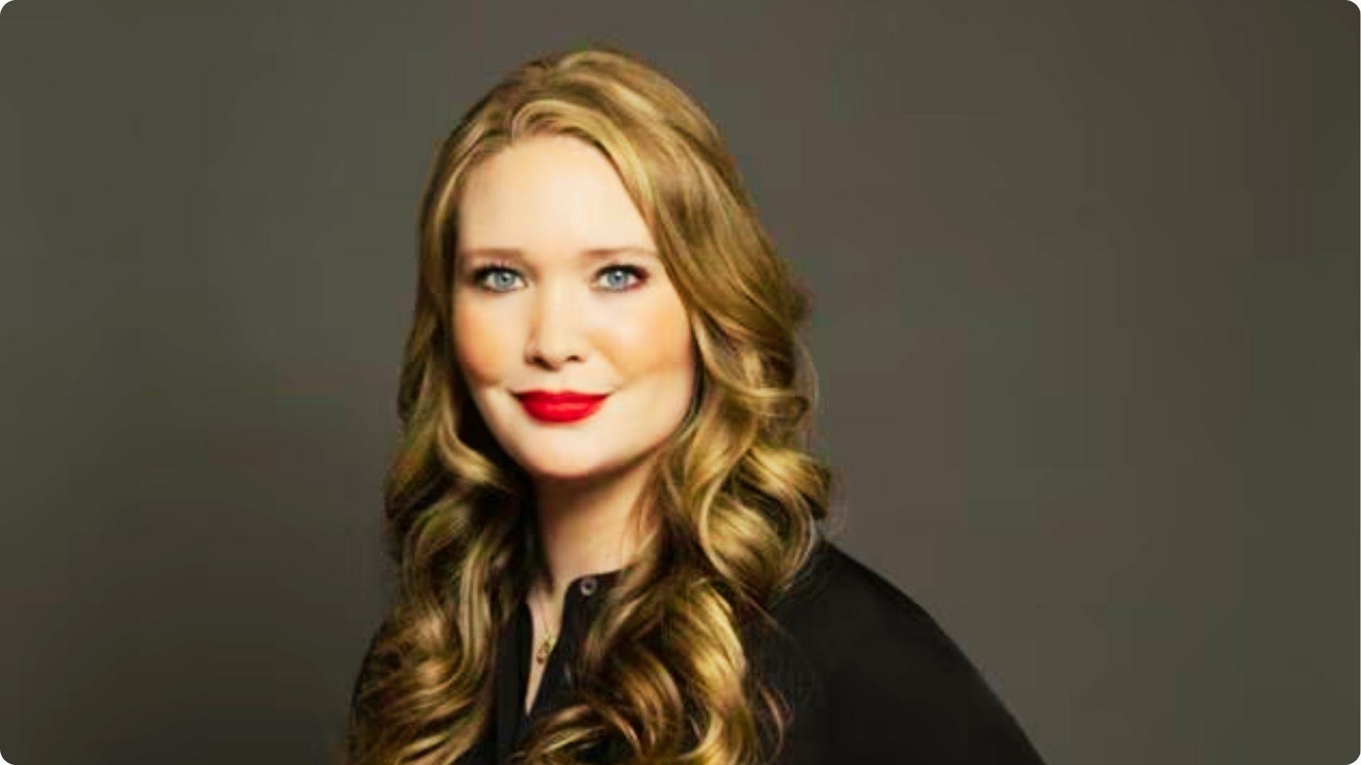 Studio portrait of a Sarah J.Mass with wavy hair and red lipstick wearing a black top.