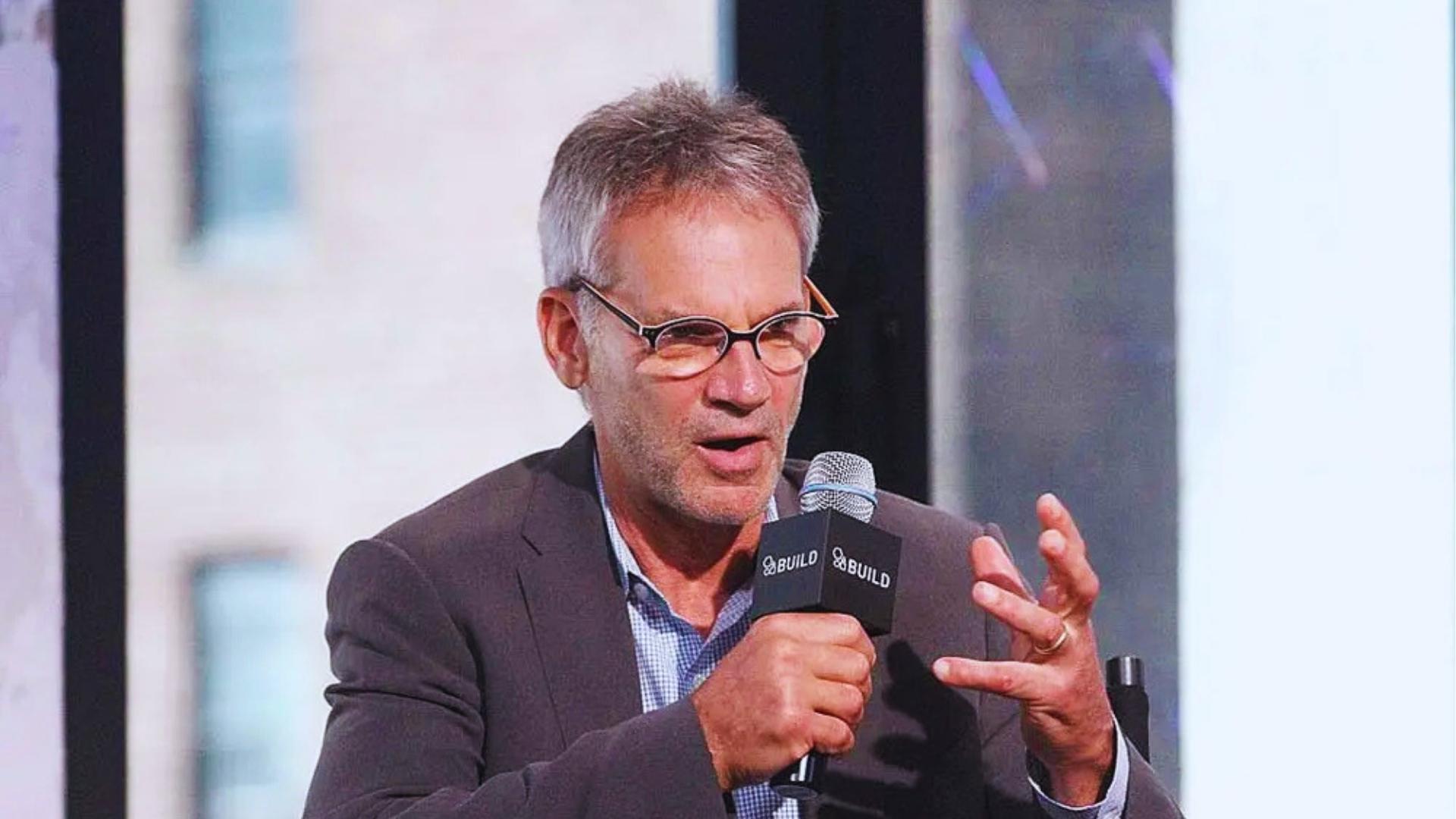 Author Jon Krakauer in gray blazer and glasses speaks into BUILD microphone, gesturing during interview about Into the Wild.