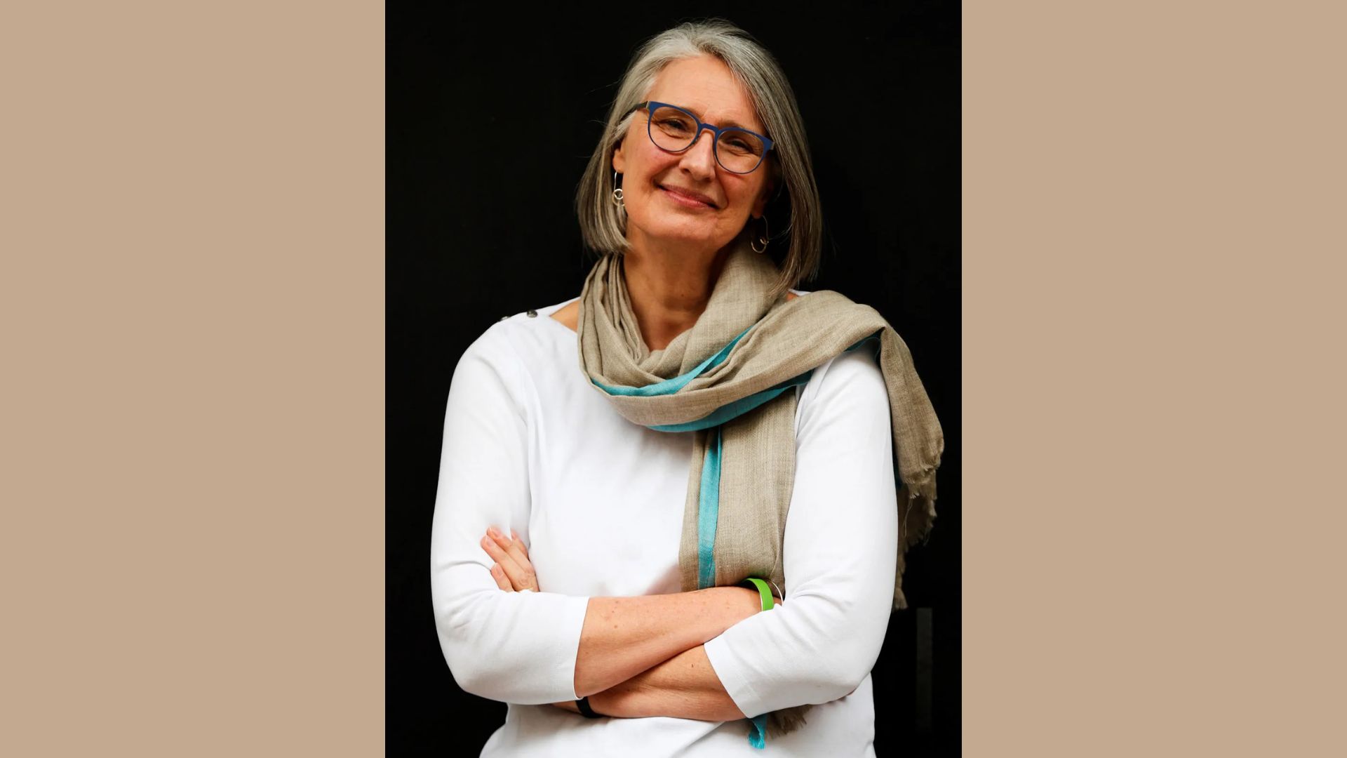 Louise Penny wearing glasses and a colorful scarf, smiling gently at the camera.