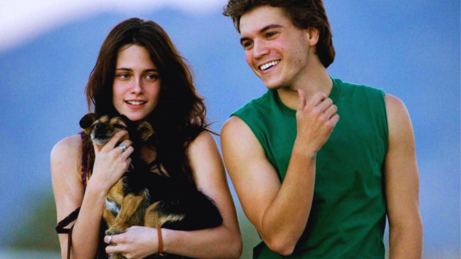 Film still from Into the Wild showing Kristen Stewart holding a small dog beside smiling Emile Hirsch as Chris McCandless.