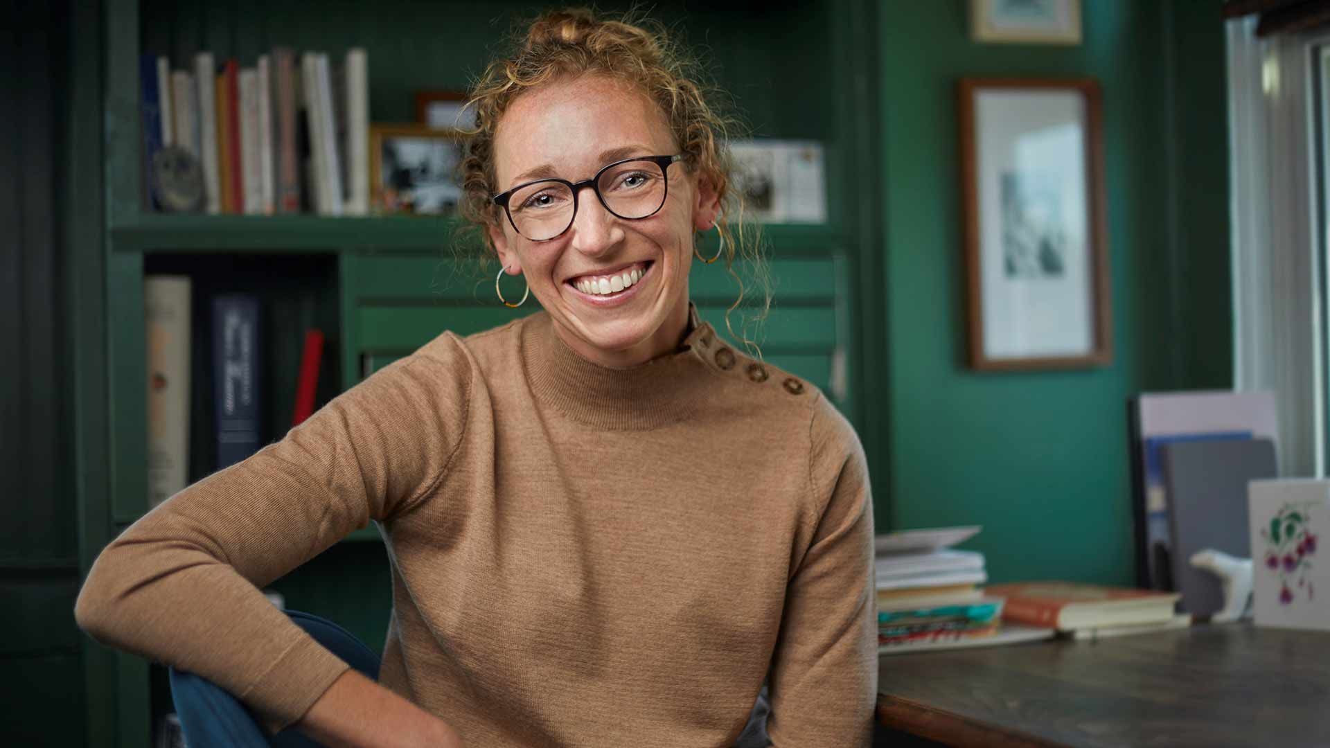 Smiling author with glasses in cozy home office, surrounded by books, for The Correspondent character summary and honest review.<